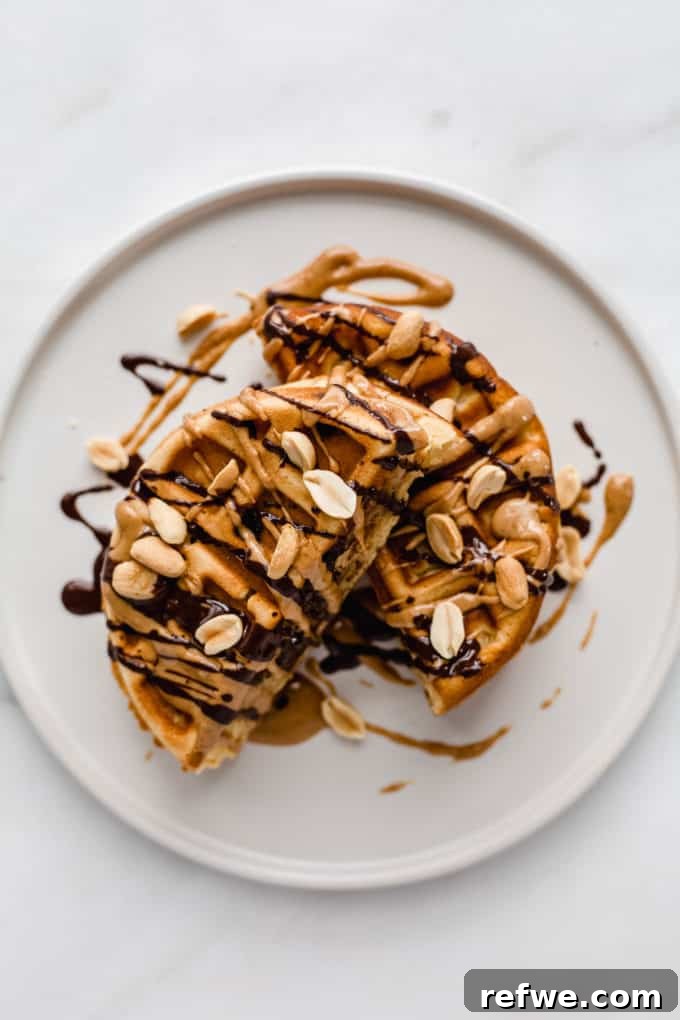 Snickers Banana Bliss Waffles 2 A perfectly cooked Banana Snickers Stuffed Waffle, sliced in half to reveal its rich banana, peanut butter, and chocolate filling, artfully drizzled with more chocolate and peanuts on a white plate.