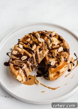A waffle cut in half on a plate topped with drizzled peanut butter and chocolate