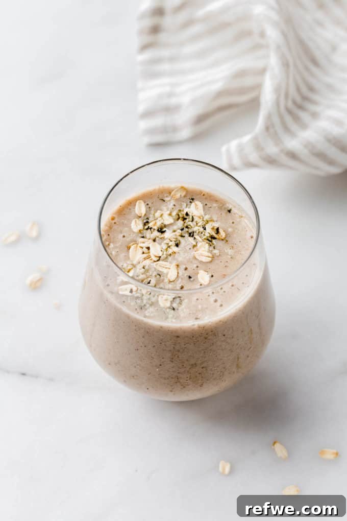 Liquid Banana Bread 2 A delicious banana bread smoothie in a glass on a marble counter, garnished with oats and a banana slice.
