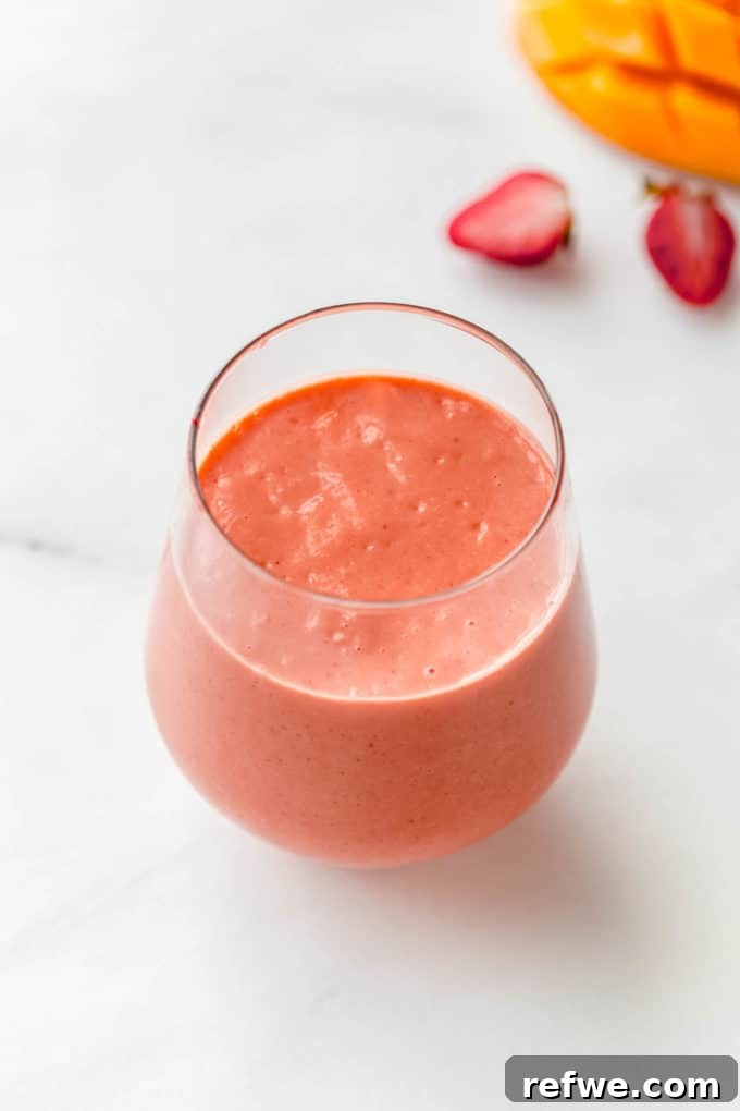 Tropical Strawberry Mango Delight 6 A beautifully prepared glass of strawberry mango smoothie, adorned with a straw, resting on a pristine marble counter, inviting a refreshing sip.