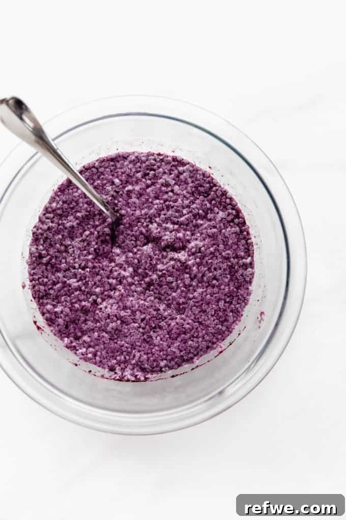 A clear mixing bowl filled with a creamy, vibrant purple blueberry chia pudding mixture, showing its smooth and even texture after being thoroughly combined, ready for chilling.