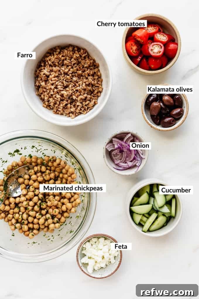 Mediterranean Vitality Bowls 3 A flat lay of fresh, colorful ingredients laid out for a Greek power bowl, including chickpeas, farro, cherry tomatoes, cucumber, olives, red onion, and crumbled feta cheese.