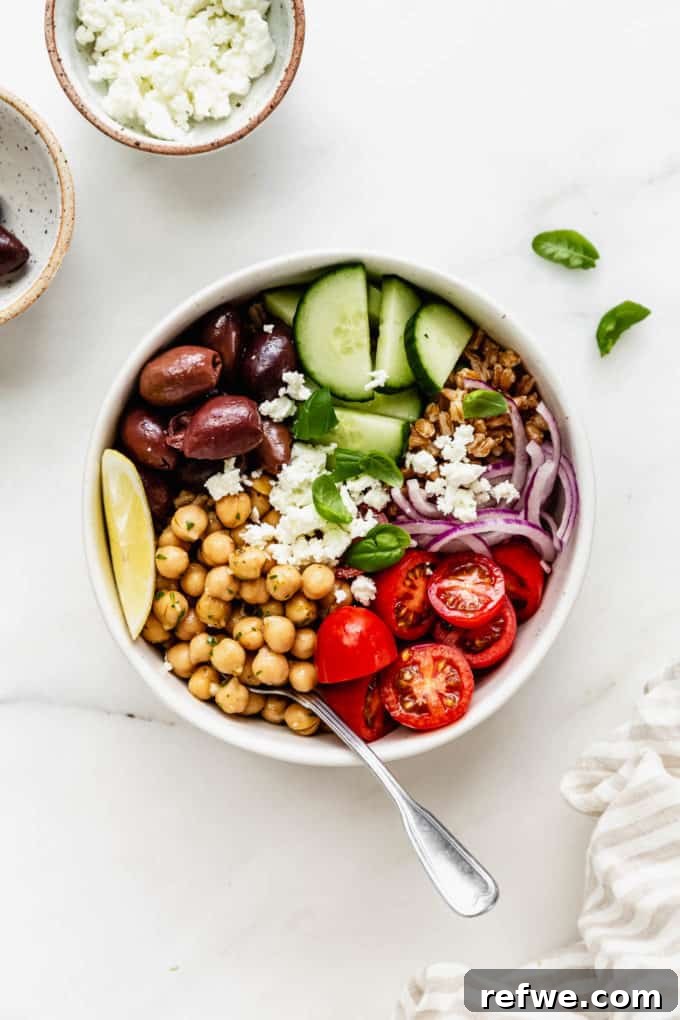 Mediterranean Vitality Bowls 6 A neatly arranged bowl with a base of cooked farro, topped with marinated chickpeas, an assortment of fresh vegetables, and a side napkin, showcasing a healthy meal.
