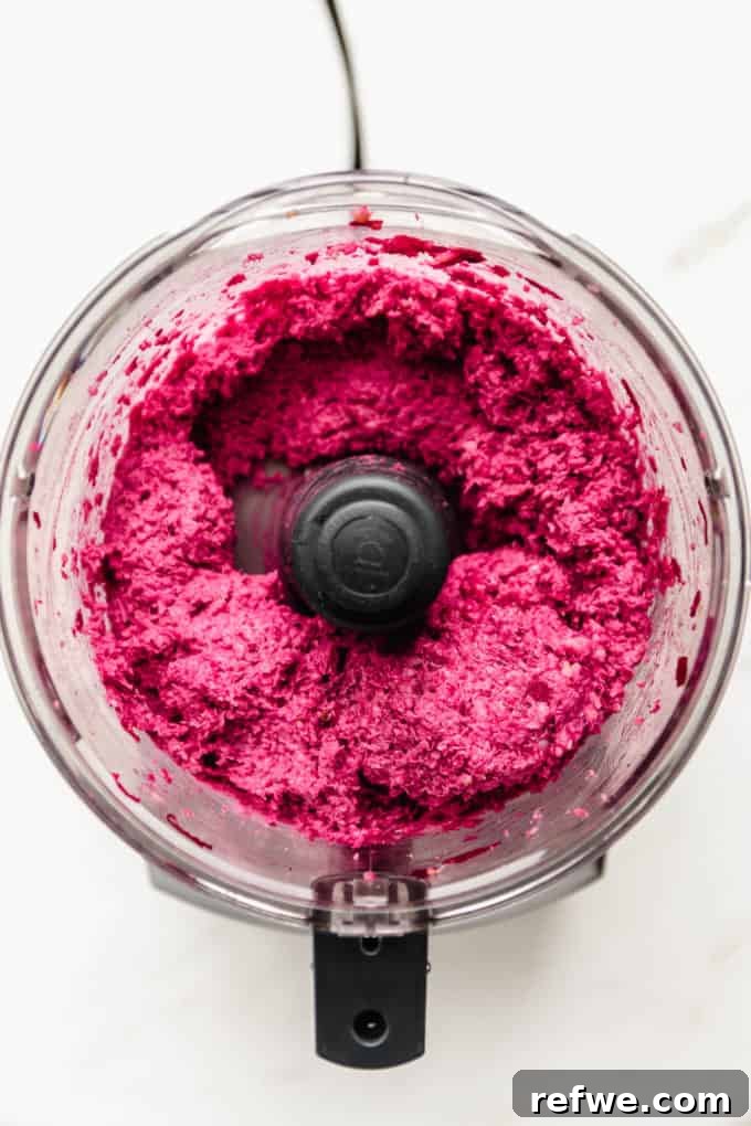 Vibrant Vegan Beet Burgers 4 A vibrant pink and textured mixture for beet burgers inside a food processor bowl after initial blending.