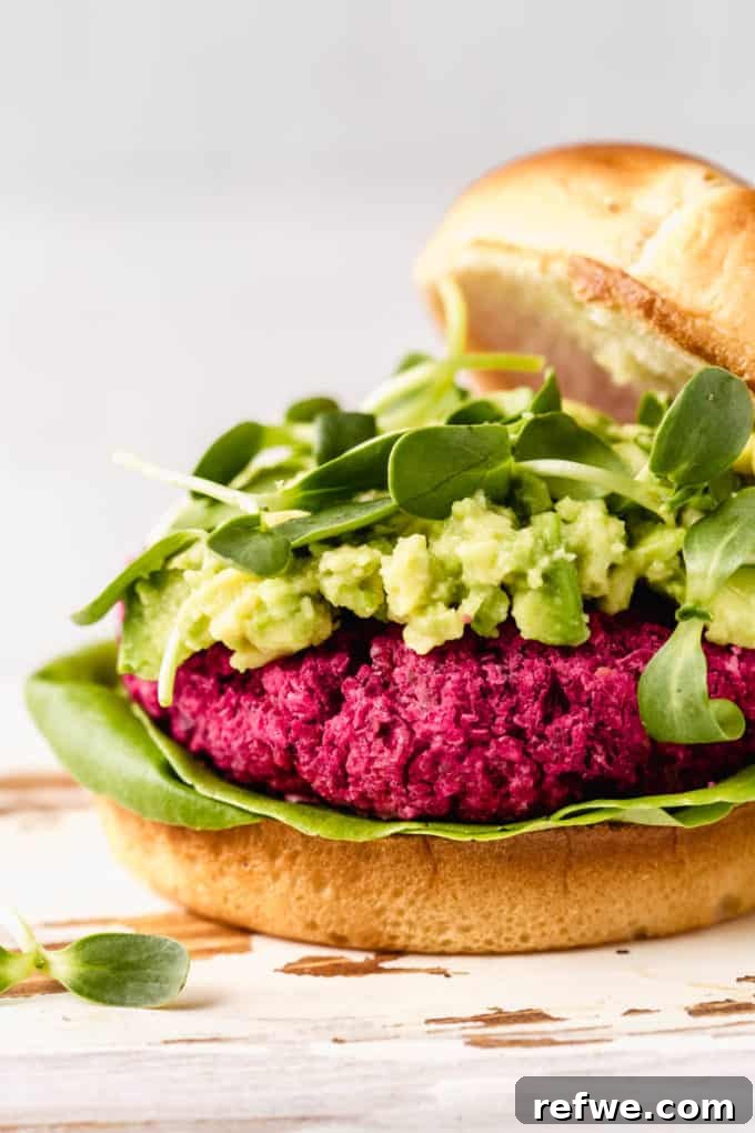 Vibrant Vegan Beet Burgers 6 A close-up view of a perfectly cooked vegan beet burger, topped with creamy mashed avocado and fresh sprouts, served on a bun.