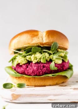 A perfectly assembled vegan beet burger in a bun, layered with fresh avocado, vibrant sprouts, and crisp lettuce.