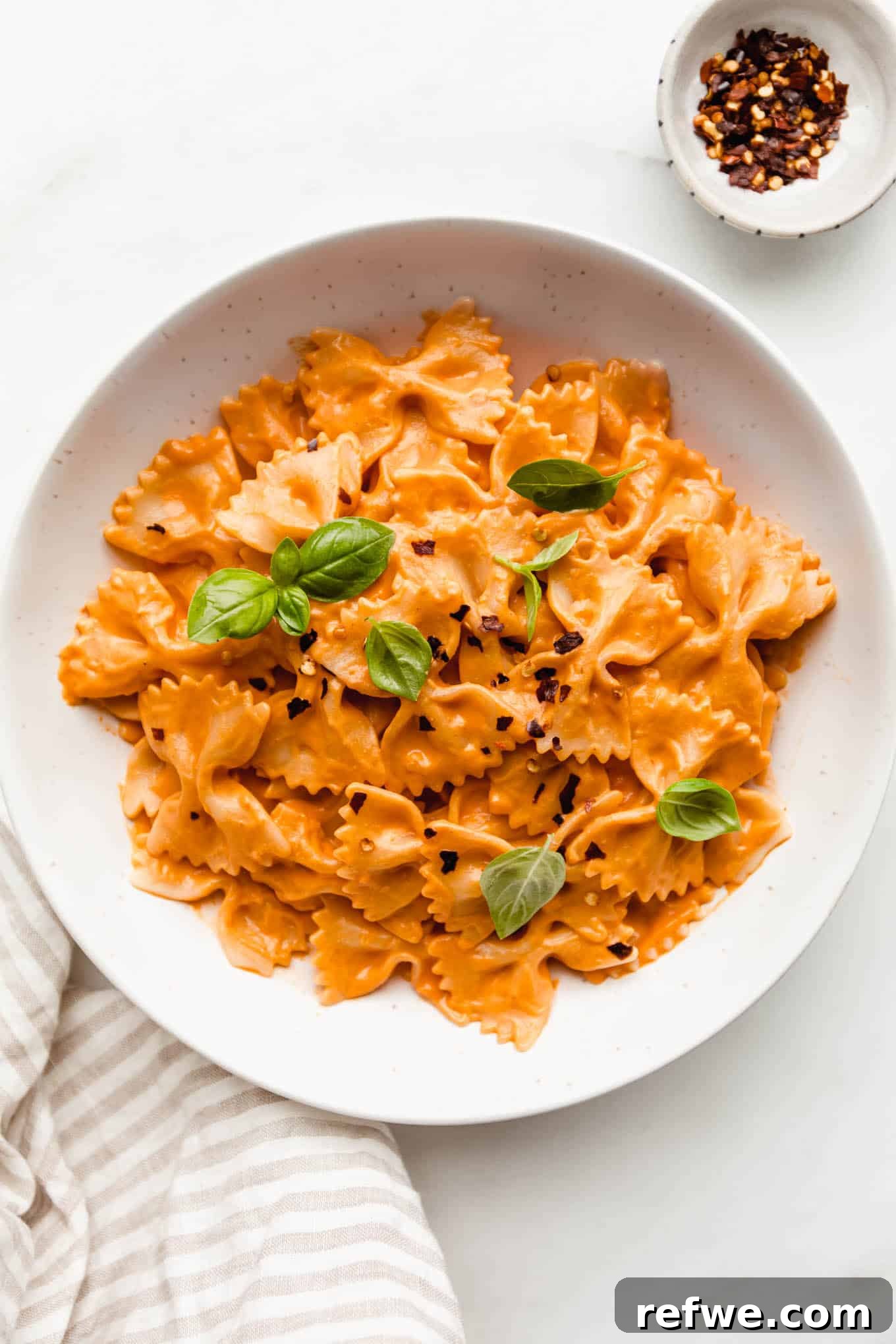 Velvety Vegan Vodka Pasta 2 A beautifully plated bowl of creamy vegan vodka pasta, garnished with fresh basil, with chili flakes and a napkin in the background.