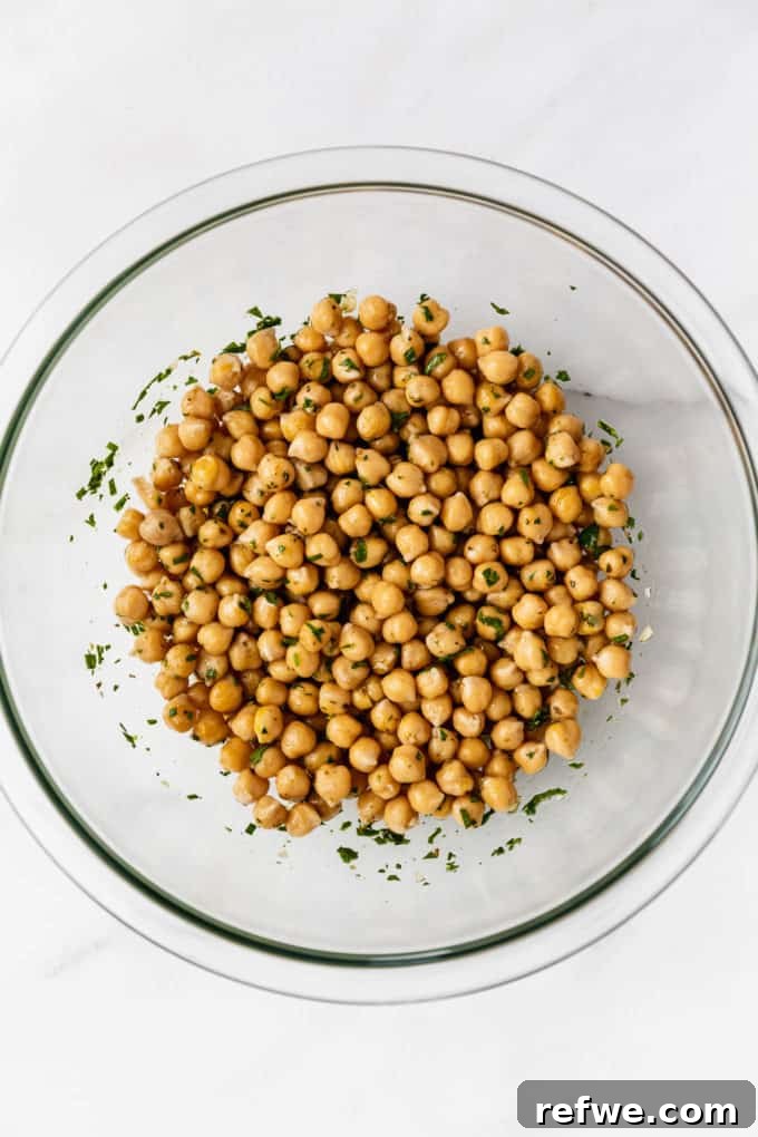 Infused Chickpea Bites 4 A clear glass mixing bowl prominently displaying freshly marinated chickpeas, glistening with the herbaceous dressing.