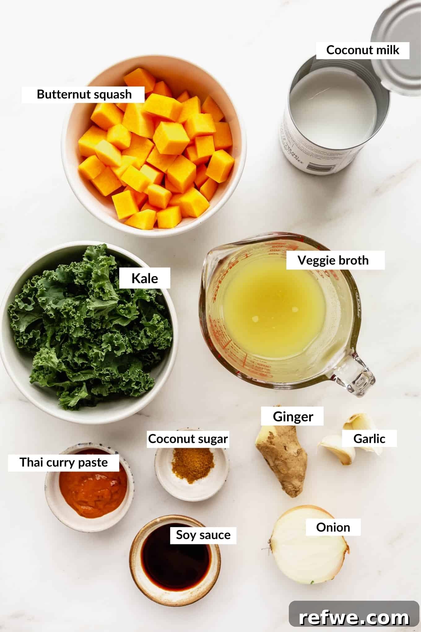 Velvet Squash Curry 3 A flat lay arrangement of fresh ingredients ready to make a butternut squash curry, including squash, kale, ginger, garlic, and coconut milk