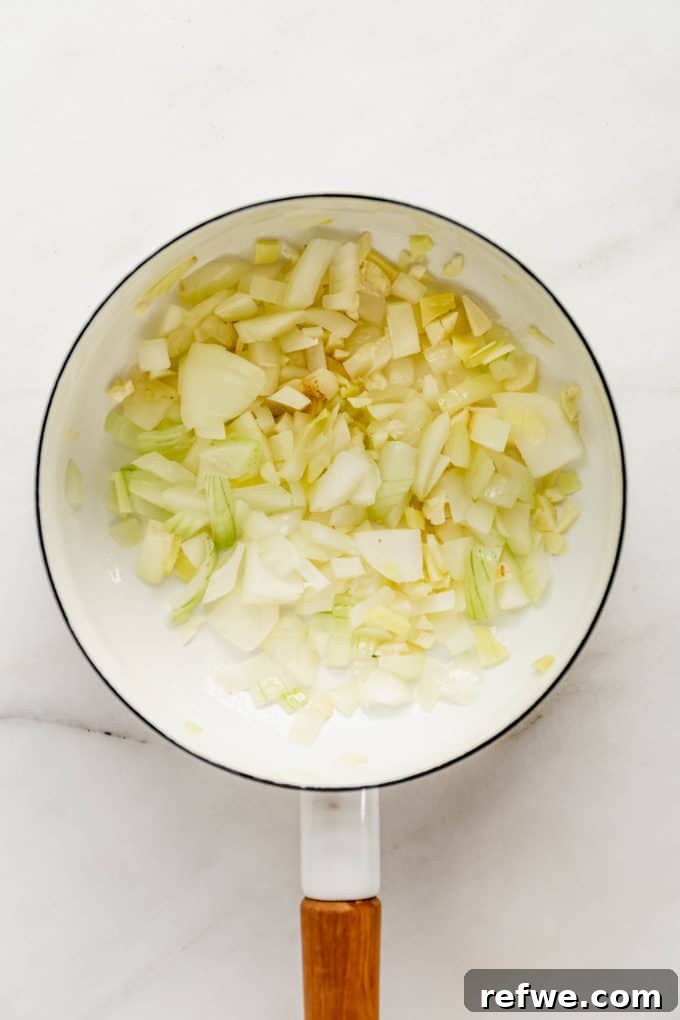 Velvet Squash Curry 4 A white pot on a stovetop with sautéing onions and garlic