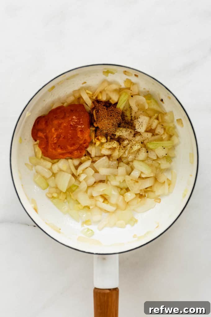 Velvet Squash Curry 5 A white pot with onions, garlic, and curry paste being stirred together