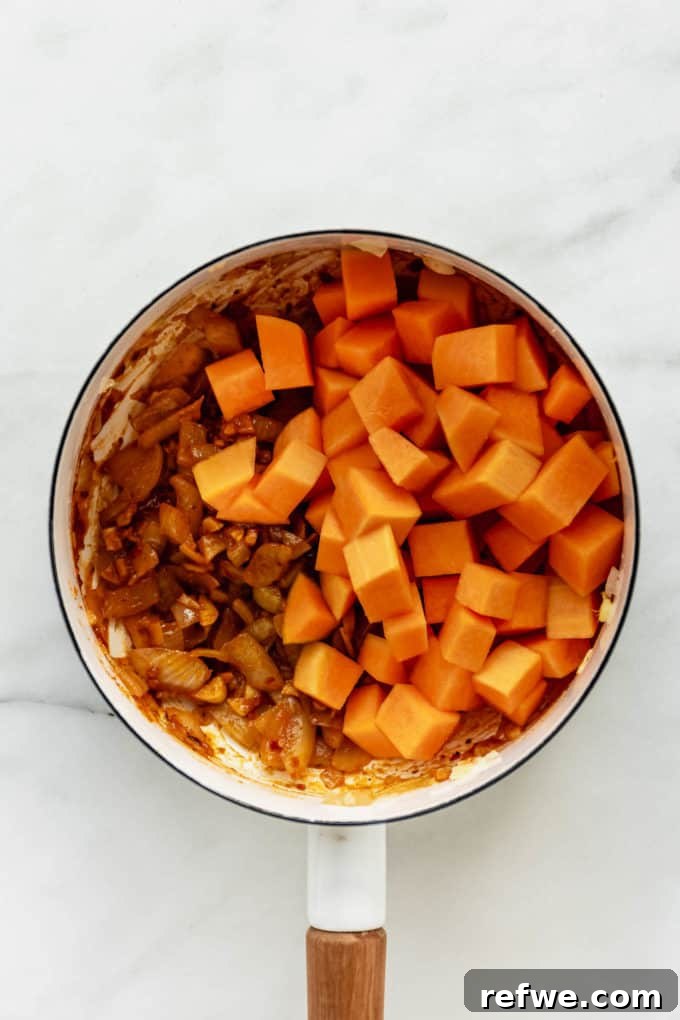 Velvet Squash Curry 6 A white pot filled with cubed butternut squash and sautéed onions