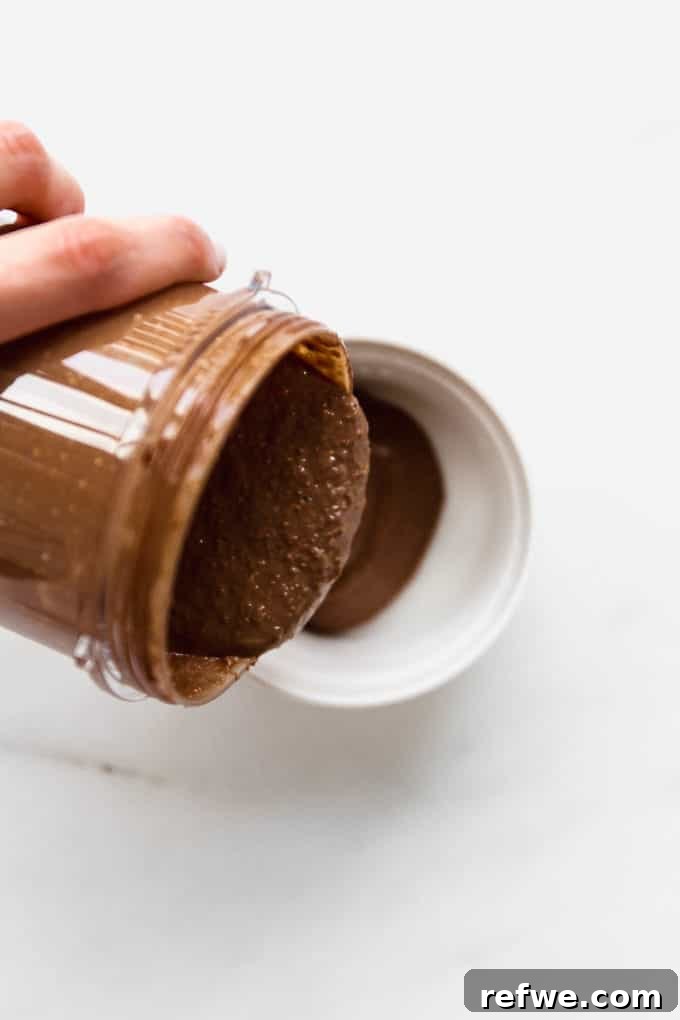 Morning Chocolate Indulgence 6 A hand pouring smooth chocolate oat batter into a small white ramekin.