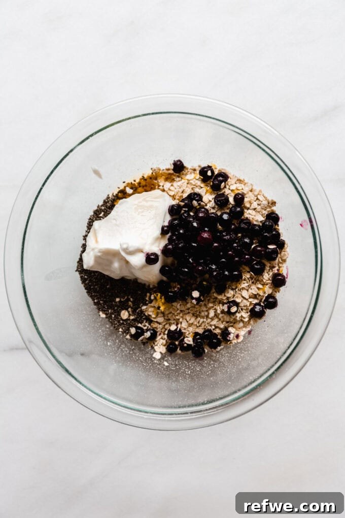 Creamy Blueberry Overnight Oats 5 Oats, yogurt, chia seeds, and fresh blueberries added to a clear mixing bowl.