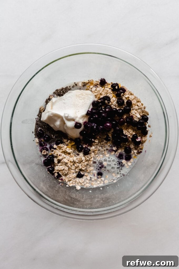 Creamy Blueberry Overnight Oats 6 Oats, chia seeds, yogurt, blueberries, and almond milk in a clear mixing bowl, ready for final mixing.