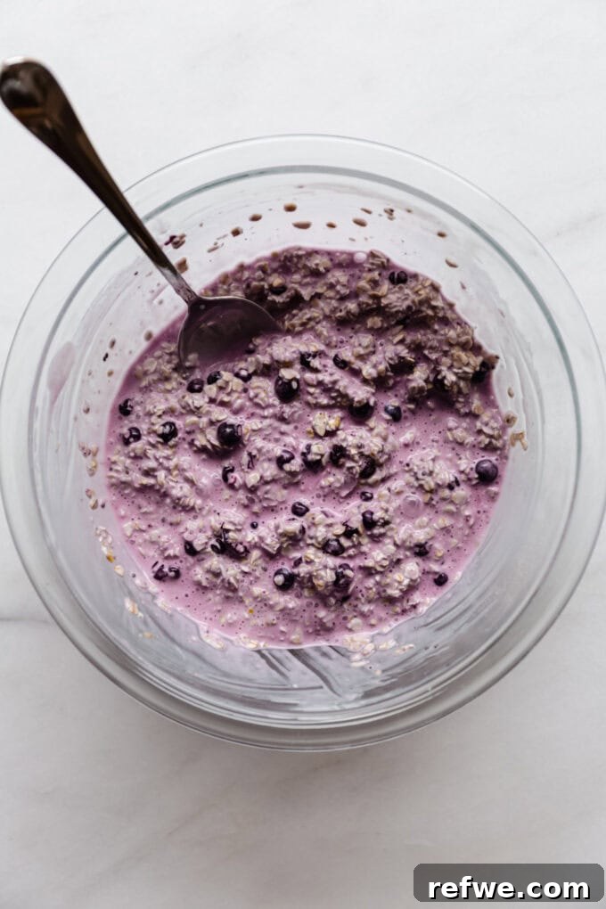 Creamy Blueberry Overnight Oats 7 Blueberry overnight oats mixture before setting in the fridge, in a clear mixing bowl with a spoon.