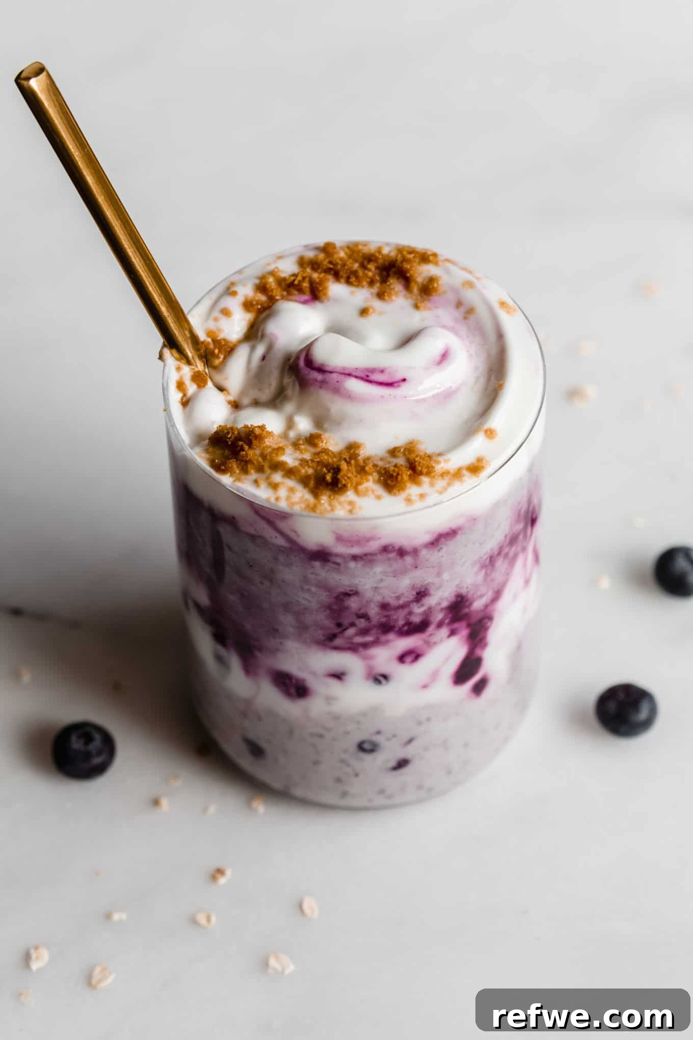 Creamy Blueberry Overnight Oats 10 Blueberry overnight oats in a stylish cup topped with yogurt, with a gold spoon invitingly placed.