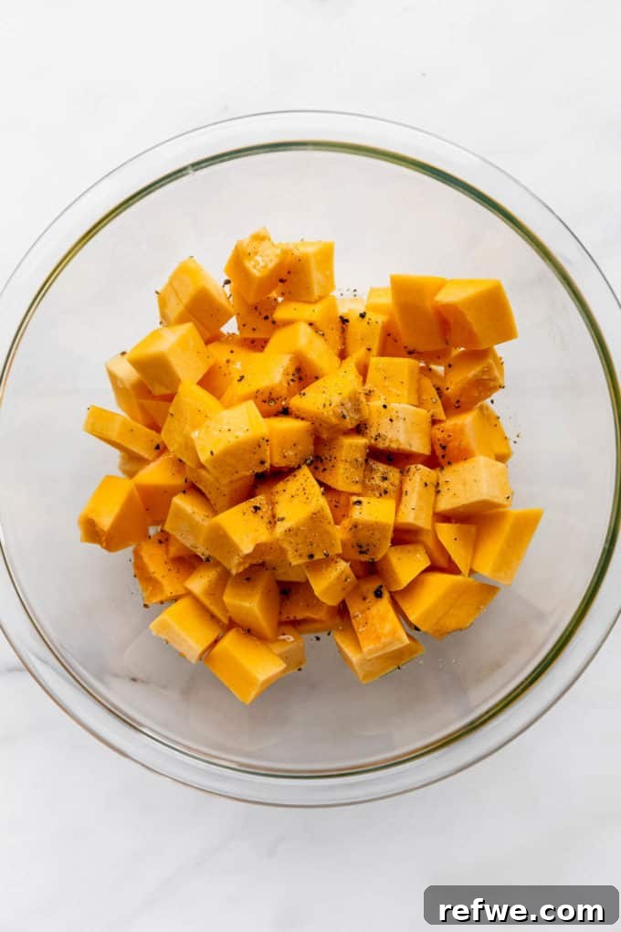 Autumn Roasted Pumpkin Salad 5 Small cubes of pumpkin coated in olive oil, salt, and pepper within a clear mixing bowl, glistening under the light.