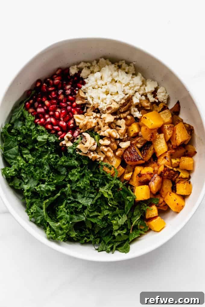 Autumn Roasted Pumpkin Salad 8 A large white mixing bowl filled with vibrant ingredients including kale, roasted pumpkin, walnuts, feta, and pomegranate, ready to be dressed.
