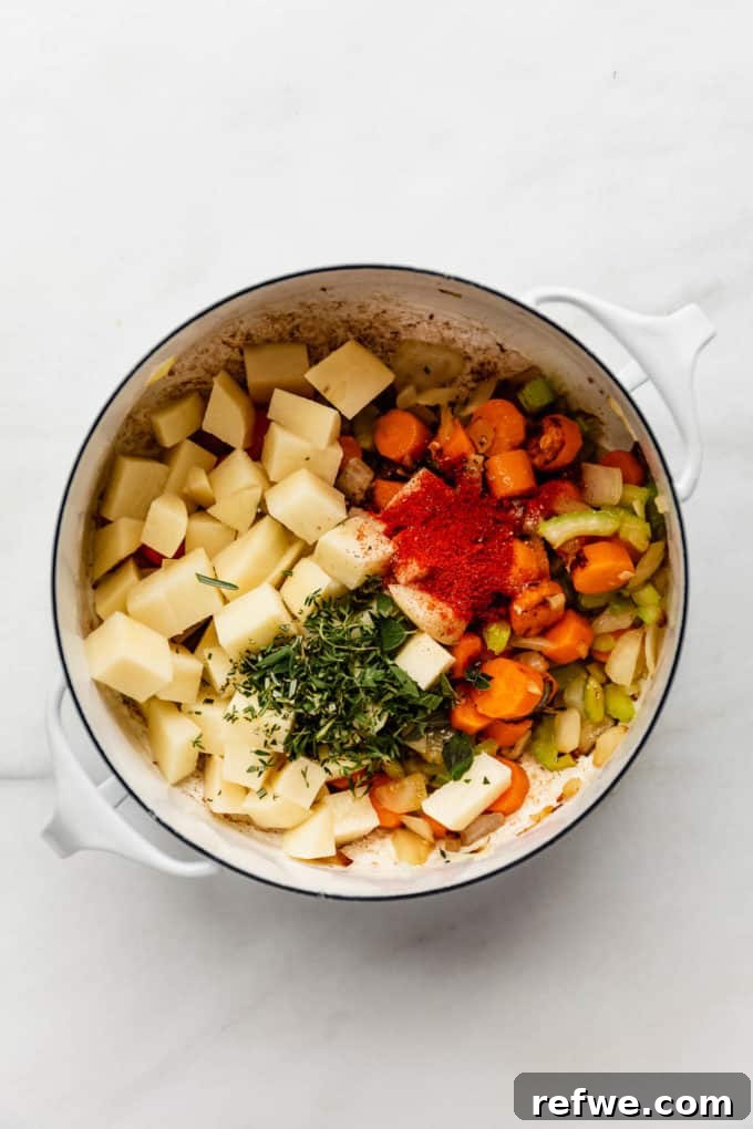 Nourishing Plant-Based Lentil Stew 5 A white pot with potatoes, vegetables, and herbs mixed in