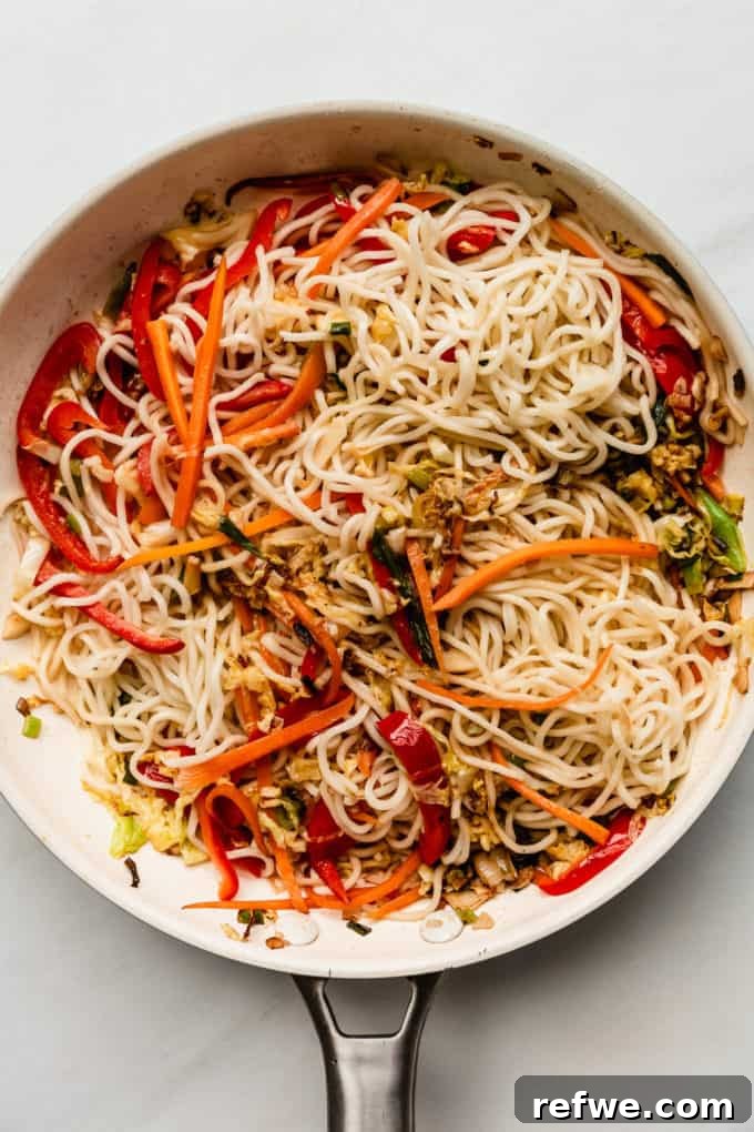 Plant-Based Vegetable Noodle Stir-Fry 8 Noodles and vegetables are thoroughly coated in sauce, stir-fried in a white pan, developing a slight crispness.