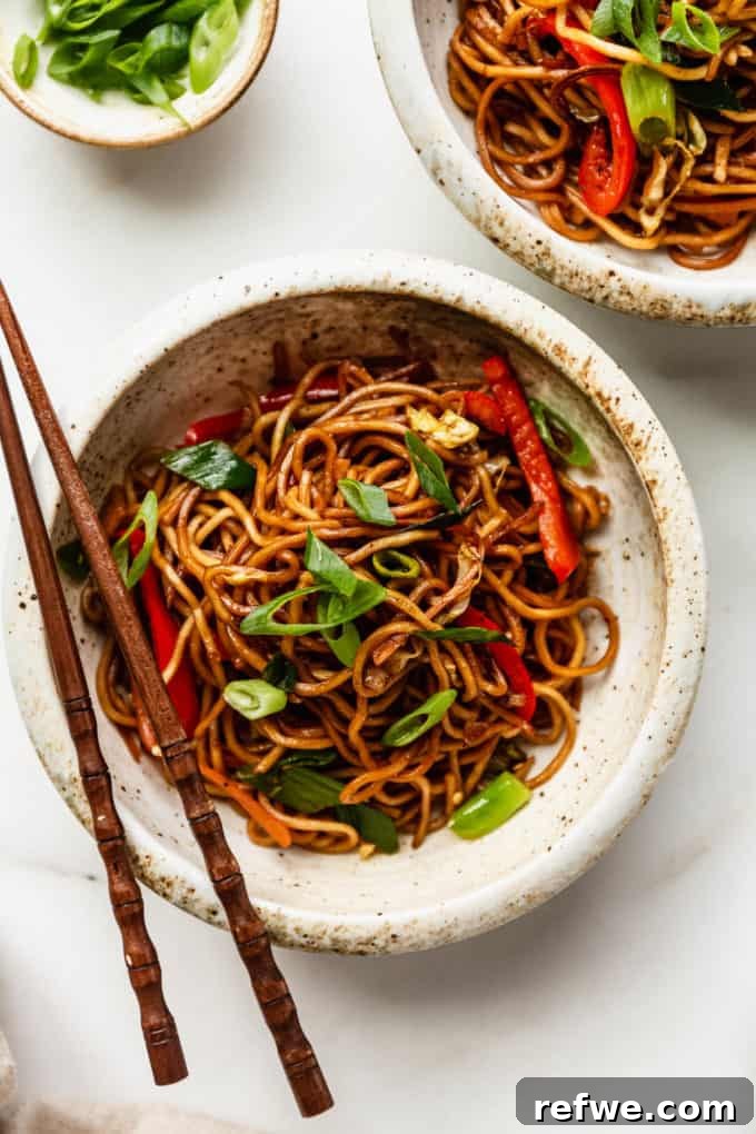 Plant-Based Vegetable Noodle Stir-Fry 10 A beautifully plated bowl of vegan chow mein, garnished with fresh green onions, with wooden chopsticks resting on top, inviting you to dig in.