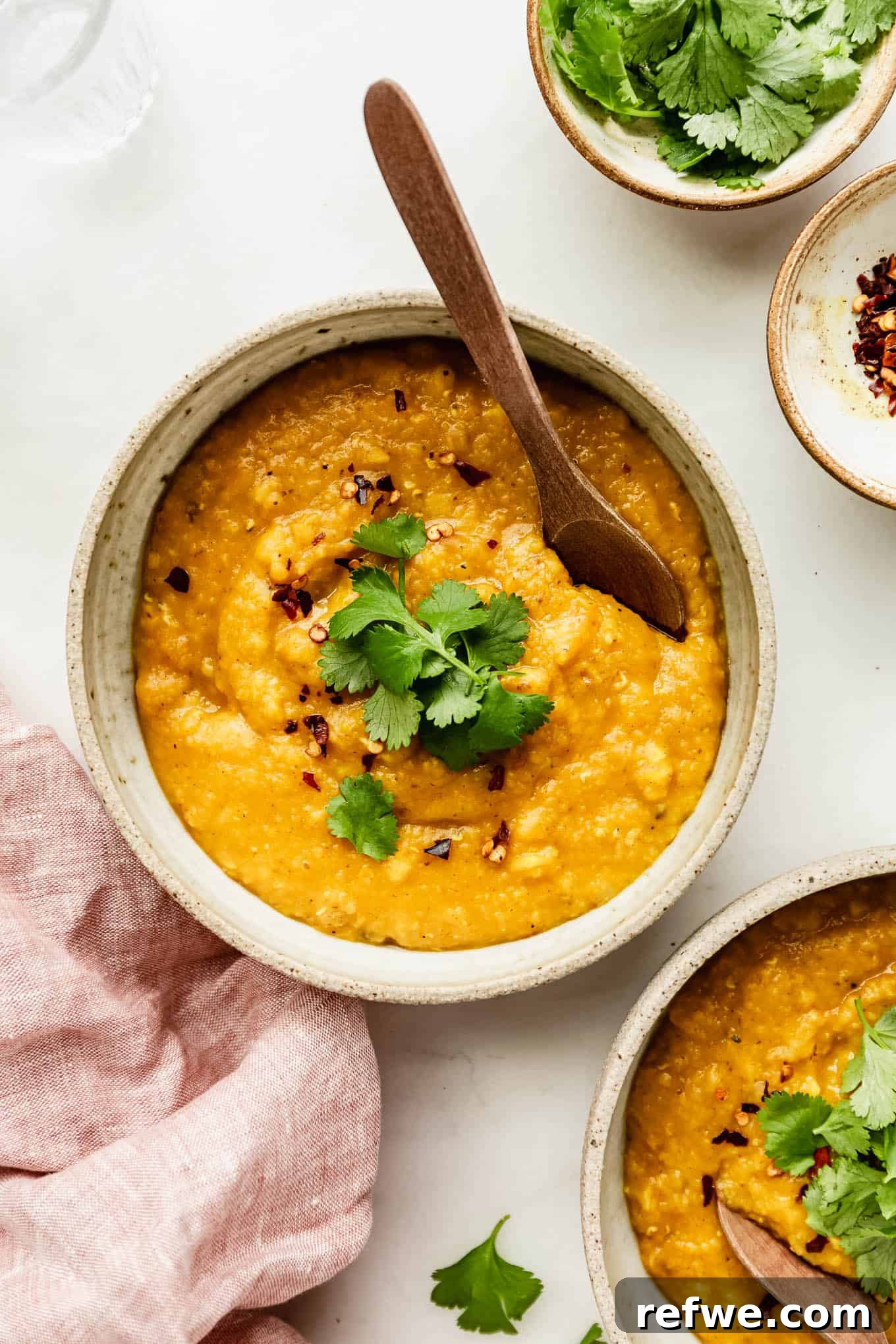 A bowl of red lentil dahl topped with fresh cilantro, ready to be served, with a pink napkin on the side.