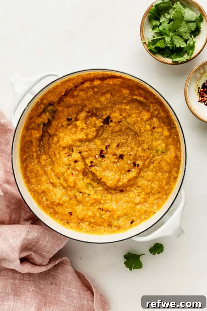 The finished red lentil dahl beautifully presented in a white pot, with a pink napkin folded neatly on the side.