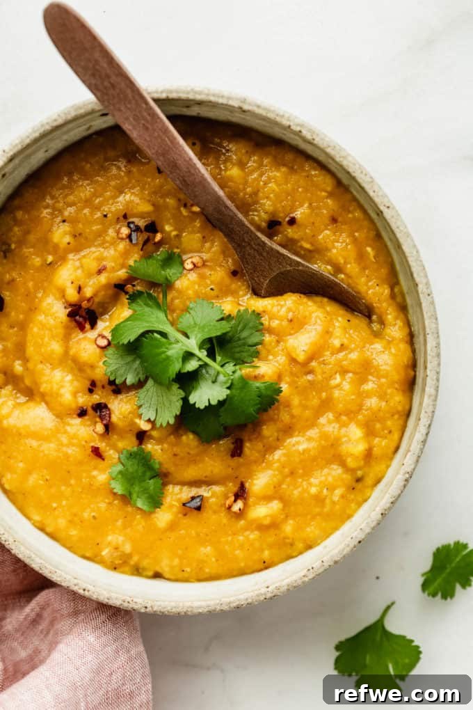 A bowl of rich red lentil dahl with a rustic wooden spoon dipped into it, ready to be enjoyed.