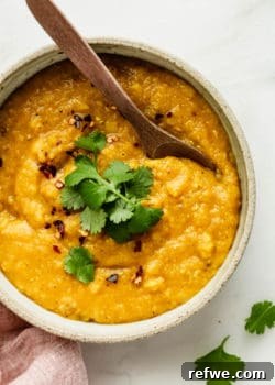 A bowl of red lentil dahl with a wooden spoon, perfect for a hearty meal.