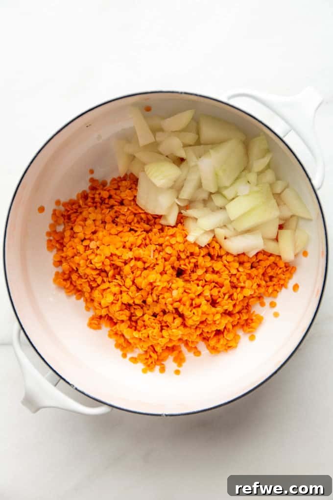 A white pot filled with vibrant red lentils and finely chopped onions, ready for cooking.