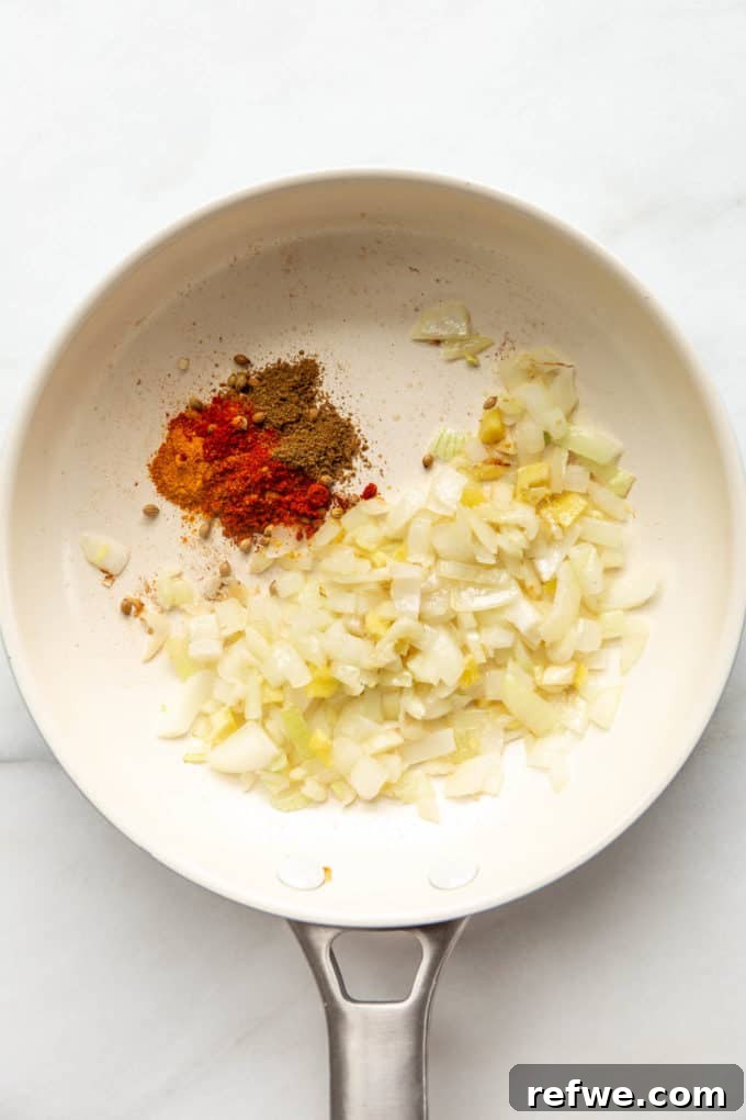 A white pan containing sautéing onions, garlic, and ginger, forming the aromatic base for the dahl.