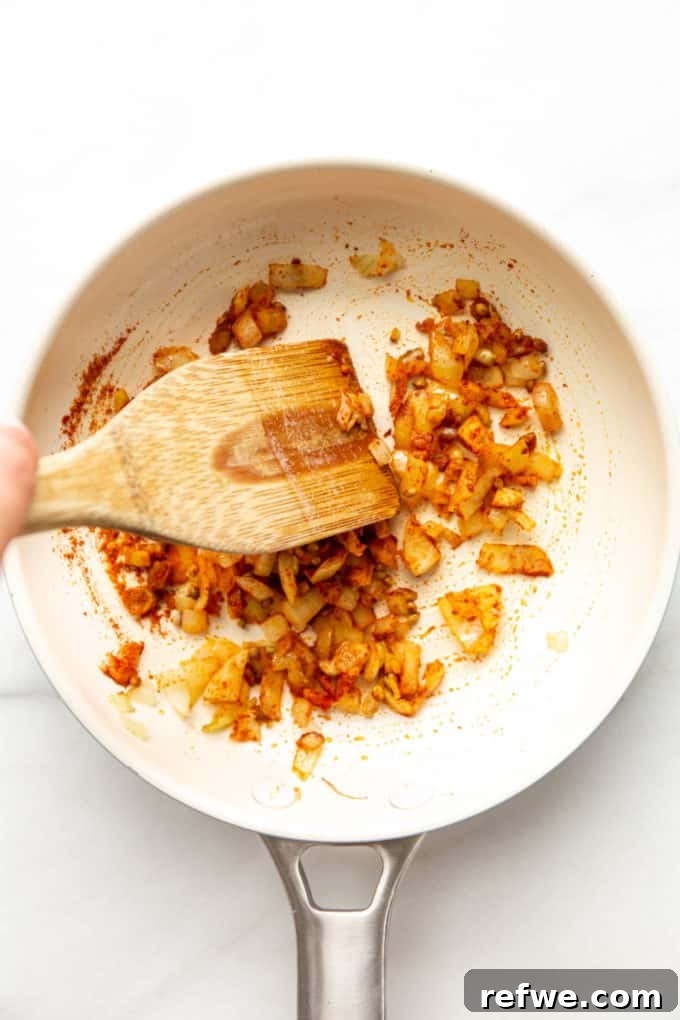 A close-up of the white pan showing onions, garlic, ginger, and various spices mixed and toasting together.