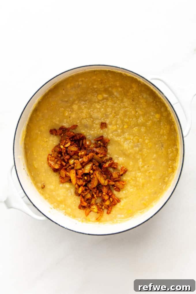 The spice mixture, with onions and other aromatics, being added to the pot of creamy red lentils.