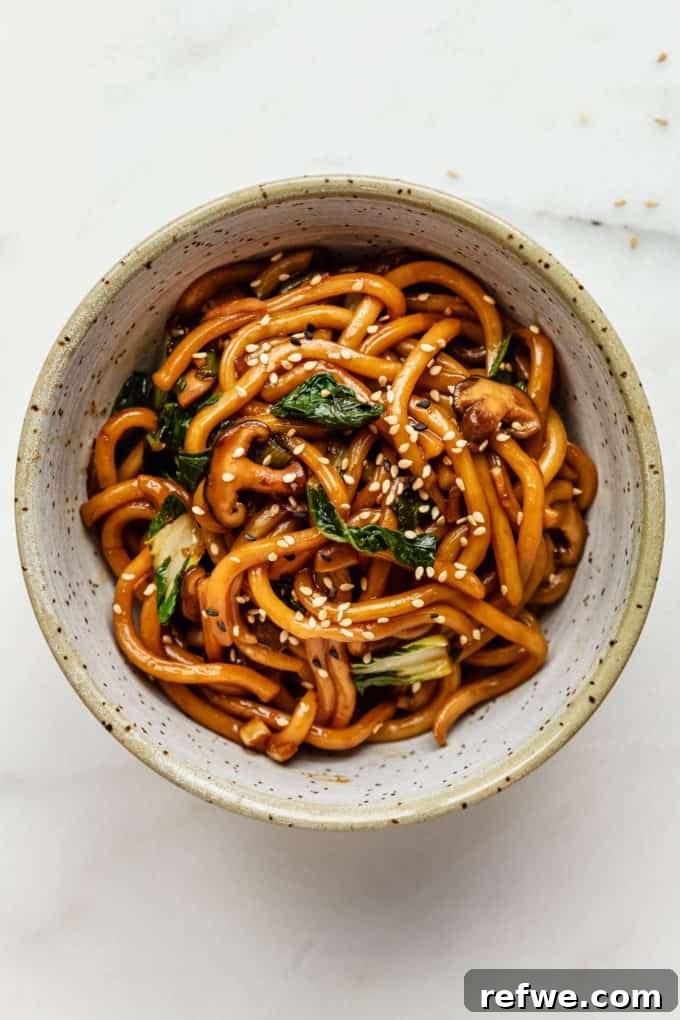 Fast and Simple Yaki Udon Stir Fry 2 A steaming bowl of Yaki Udon noodles garnished with sesame seeds and fresh scallions, ready to be enjoyed.