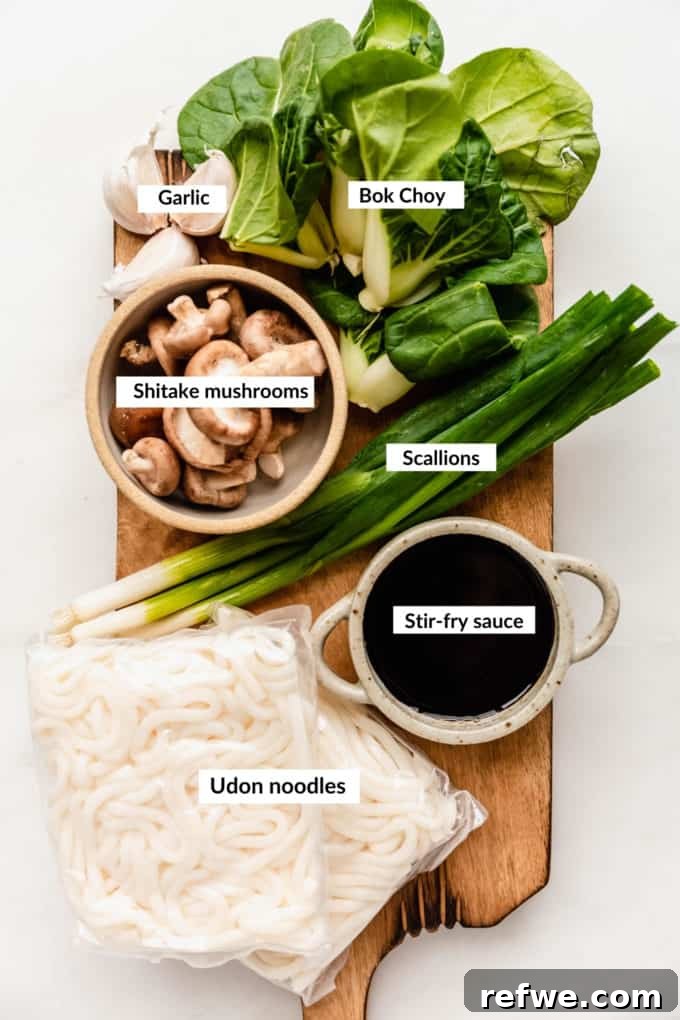 Fast and Simple Yaki Udon Stir Fry 3 A flat lay photograph showcasing the fresh ingredients for Yaki Udon: udon noodles, chopped scallions, minced garlic, sliced shiitake mushrooms, baby bok choy, and individual components for the stir-fry sauce in small bowls.