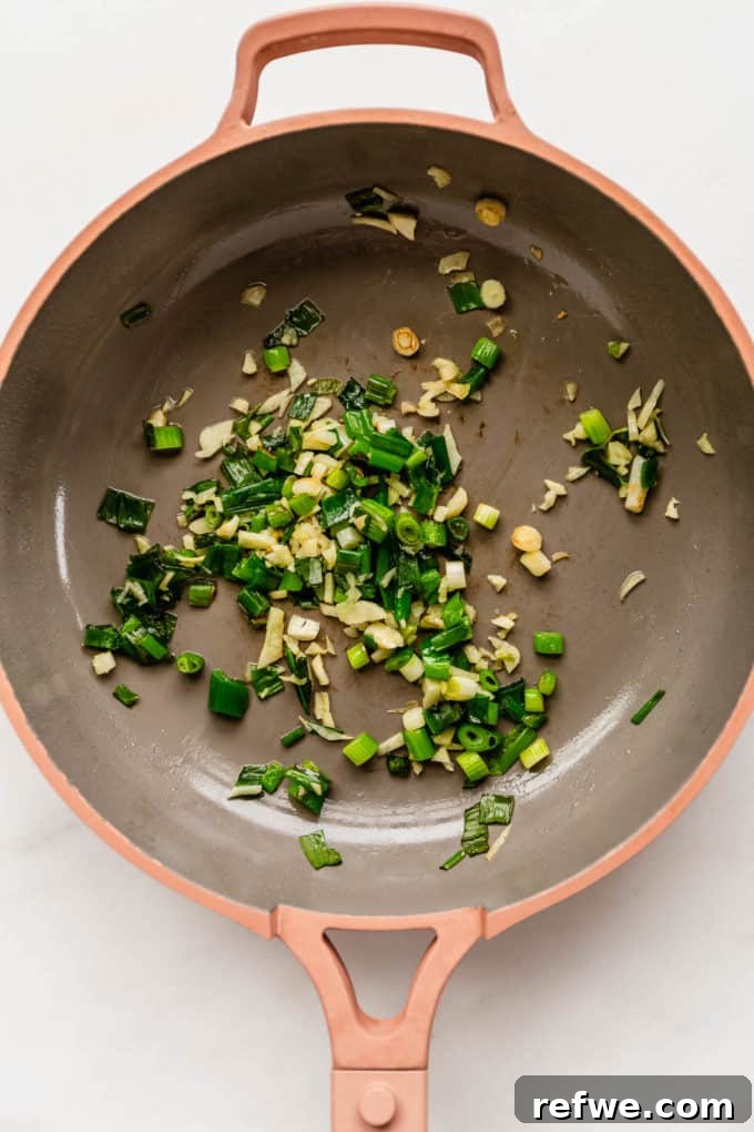 Fast and Simple Yaki Udon Stir Fry 4 Chopped scallions and minced garlic sizzling in vegetable oil in a vibrant pink pan, releasing their fragrant aroma.