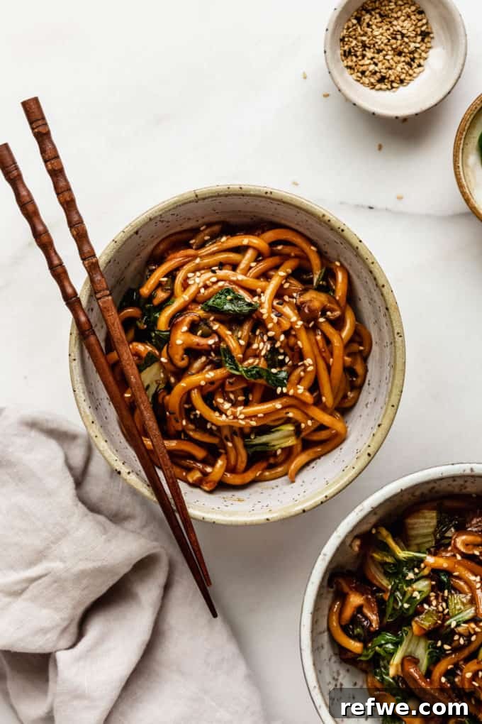 Fast and Simple Yaki Udon Stir Fry 9 Two beautifully presented bowls of Yaki Udon, garnished with sesame seeds and wooden chopsticks, arranged artfully on an elegant marble serving board.