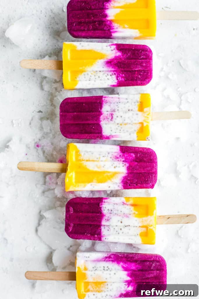 Exotic Coconut Chia Chillers 3 Six vibrant tropical coconut chia popsicles, showcasing distinct layers of golden mango, creamy white coconut, and pink dragonfruit, presented on a light background.