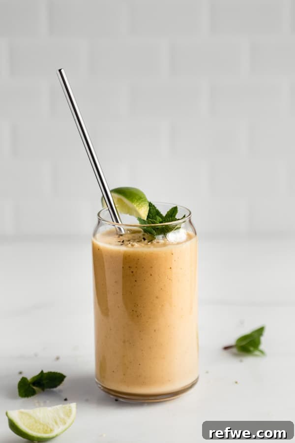 A glass of vibrant papaya mojito smoothie sits on a sleek marble countertop, bathed in soft, natural light, beautifully garnished with fresh mint leaves and a wedge of lime.