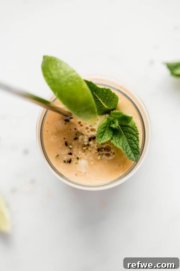 A top-down view of a refreshing papaya mojito smoothie in a glass, beautifully garnished with a vibrant lime wedge and fresh mint leaves, set against a bright backdrop.