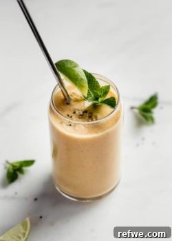 A glass of tropical papaya mojito smoothie with a metal straw, garnished with fresh mint and a lime wedge.