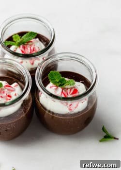 Three jars of mint chocolate pudding topped with whipped cream and crushed candy canes