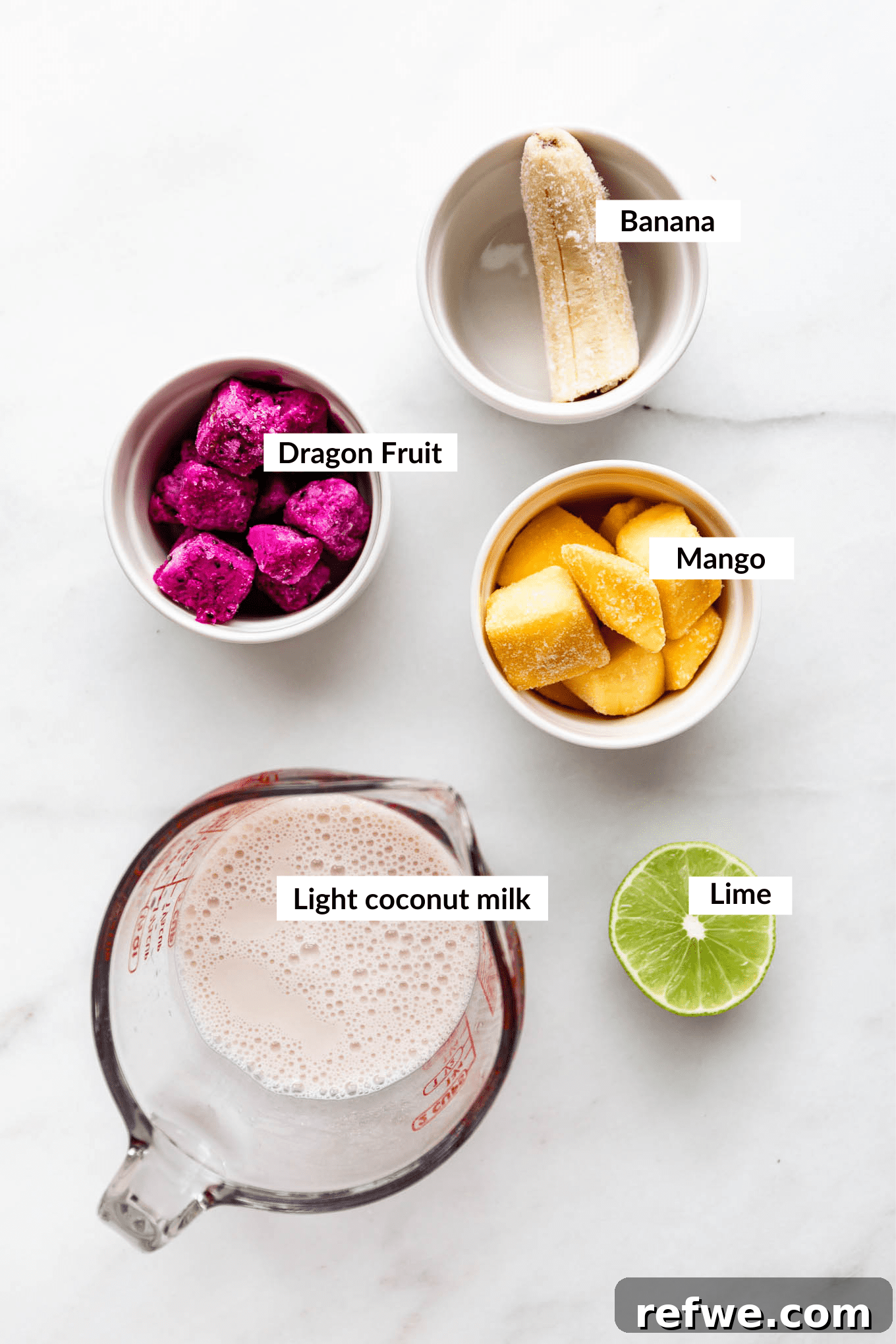 Pitaya Paradise Smoothie 3 Various fresh and frozen ingredients for a dragon fruit smoothie, including pink dragon fruit, mango, banana, and lime, laid out on a clean surface.
