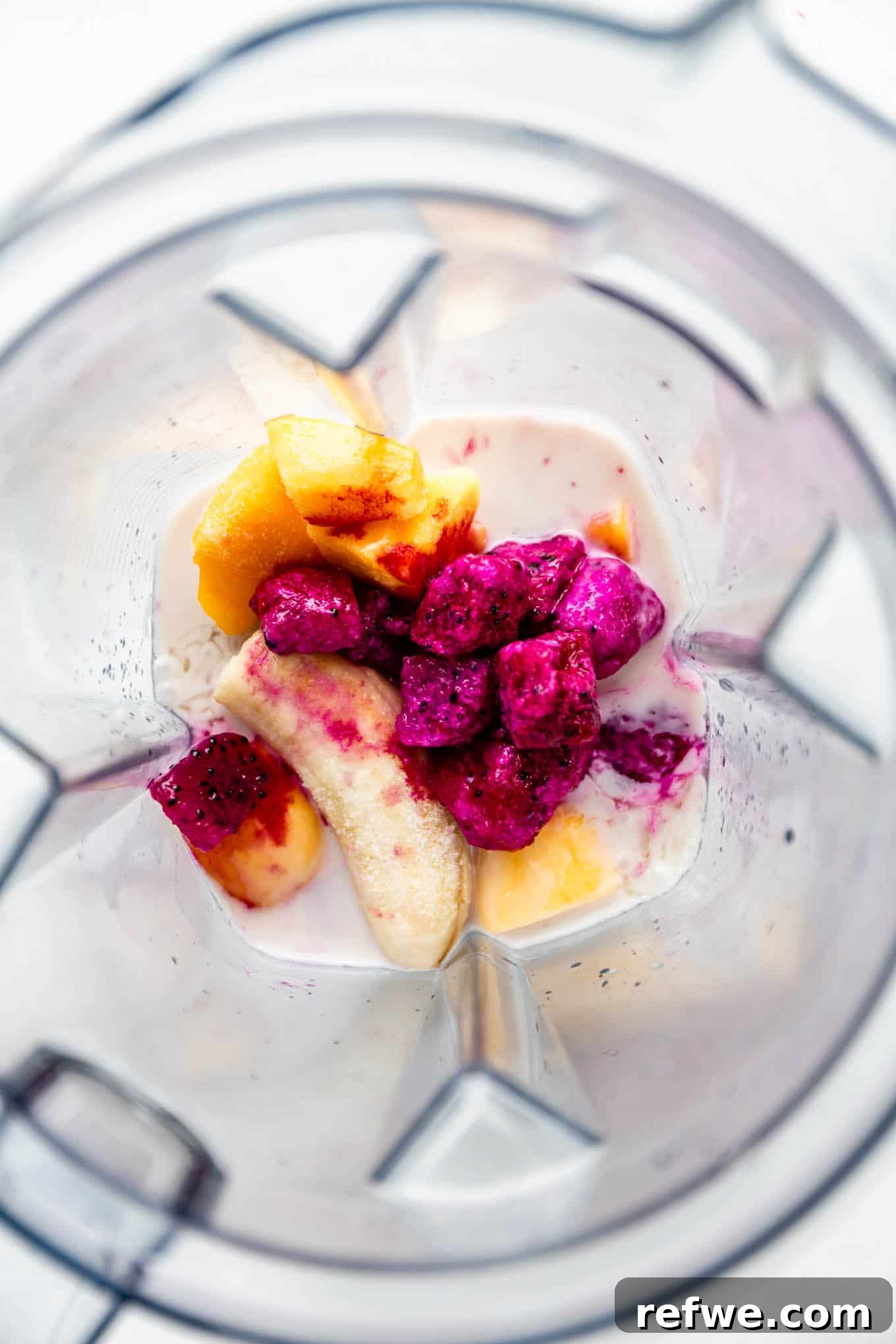 Pitaya Paradise Smoothie 4 Frozen dragon fruit, mango, banana, and coconut milk being added to a high-speed blender container.