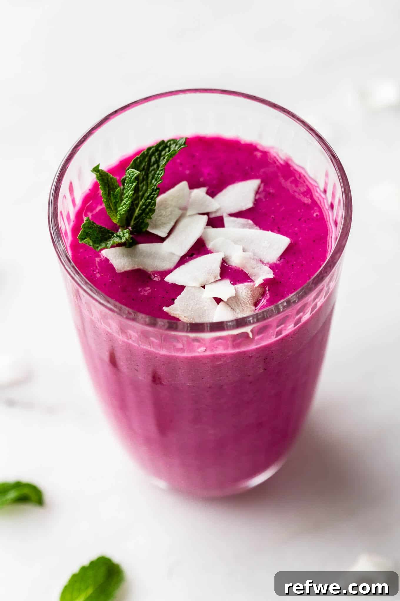 Pitaya Paradise Smoothie 6 A finished dragon fruit smoothie poured into a glass, garnished with shredded coconut and a sprig of fresh mint.