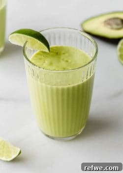 A perfectly blended avocado mango smoothie in a glass with a fresh lime wedge garnish, ready to be enjoyed.