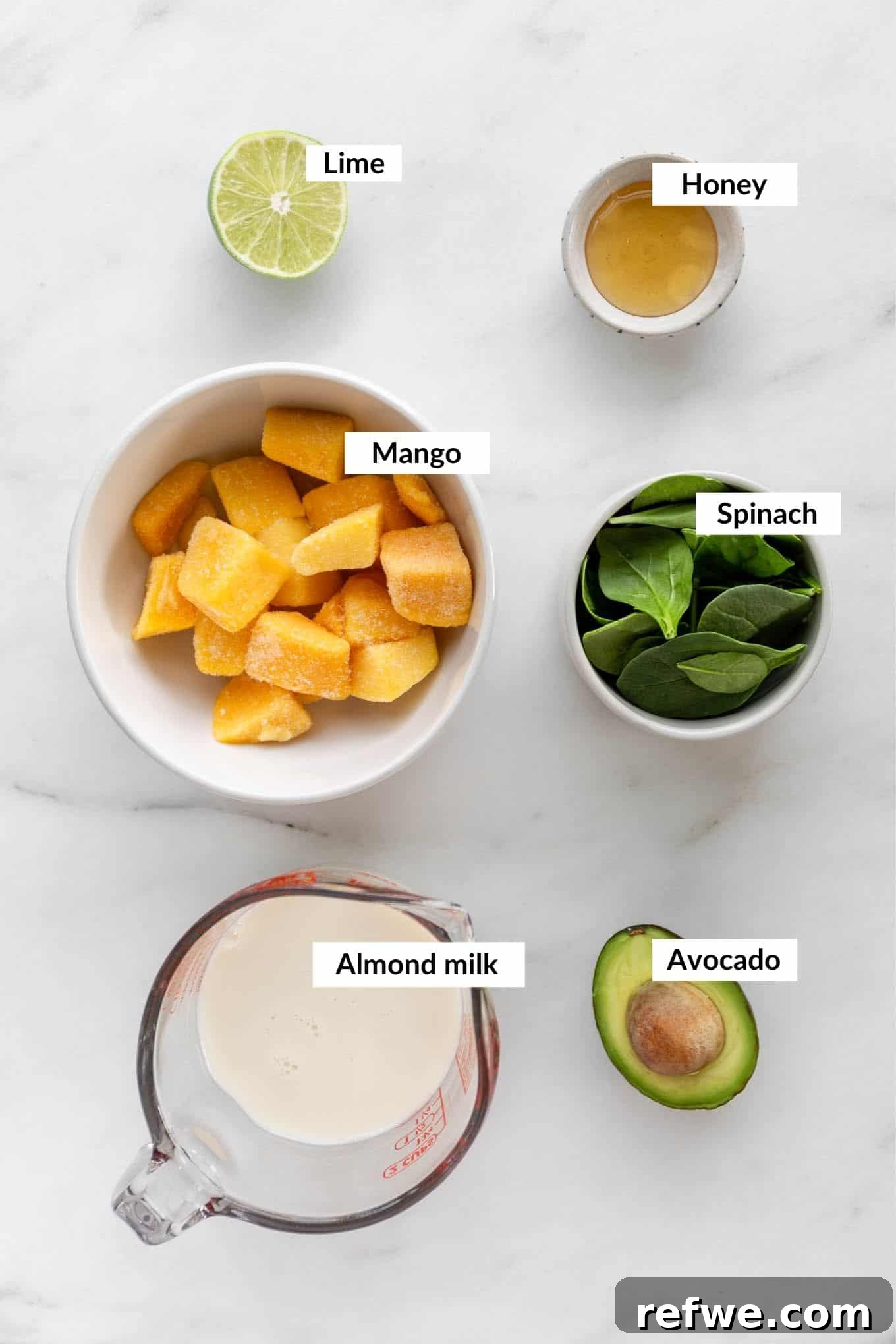 Tropical Green Dream 3 Fresh ingredients laid out on a marble surface, including ripe avocado, frozen mango cubes, fresh spinach, and a lime, all ready to be blended into a smoothie.