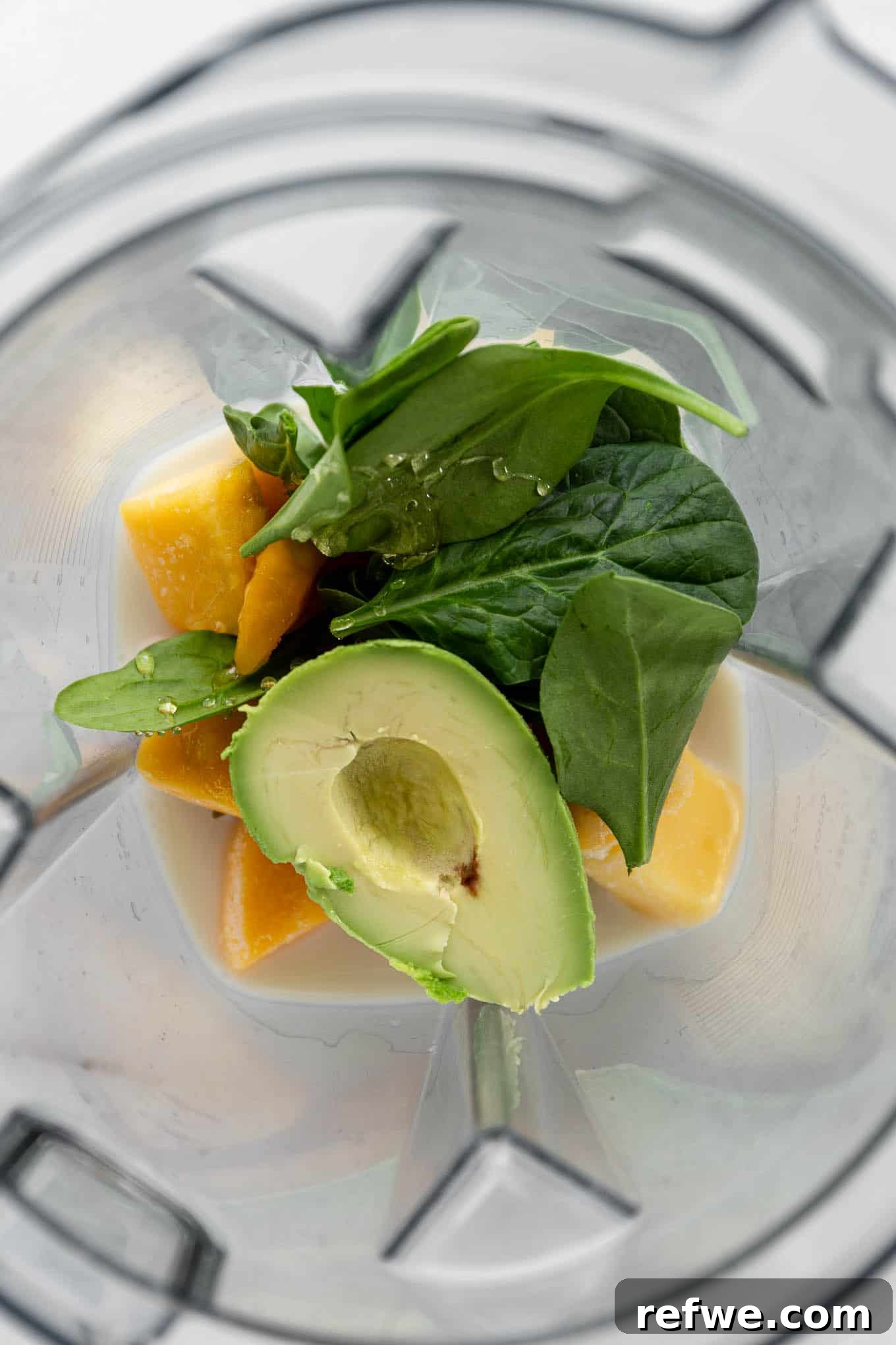Tropical Green Dream 4 A blender filled with the initial ingredients: fresh avocado, frozen mango, and vibrant spinach, ready for blending.