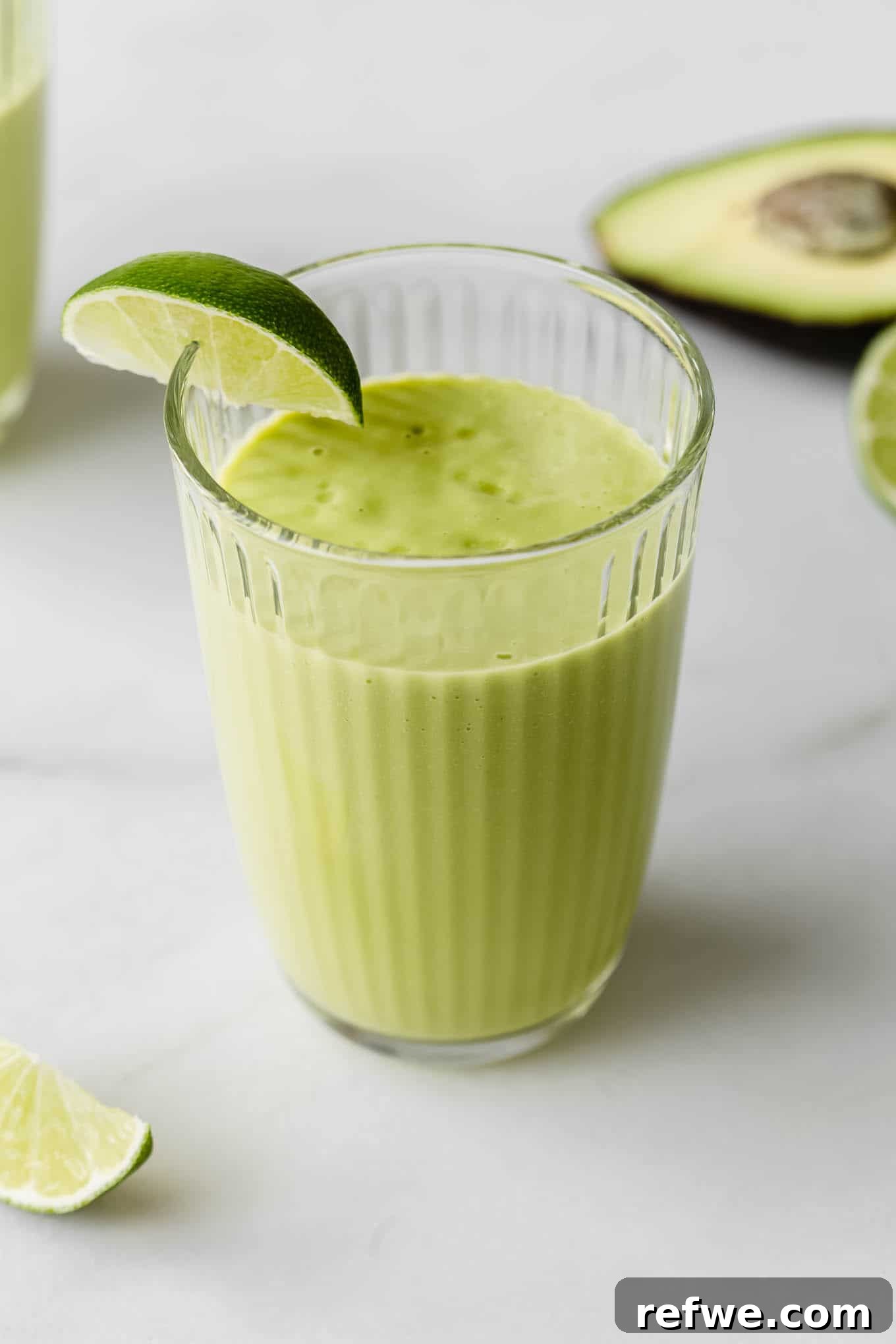 Tropical Green Dream 7 A beautifully presented avocado mango smoothie in a glass, garnished with a vibrant lime wedge, invitingly placed on a countertop.